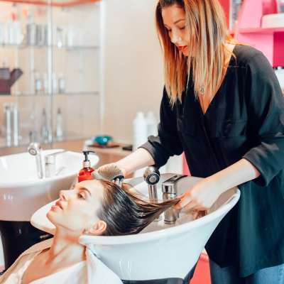 Hairdresser washes customer hair in hairdressing salon. Professional haircare in beauty studio, female client and beautician